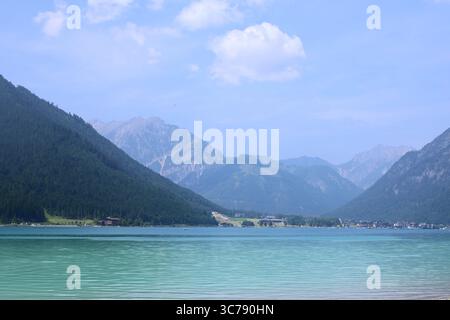 Paysage serein de turquoise lac Achensee niché parmi les montagnes boisées et rocheuses dans le Tyrol, Autriche. Une journée d'été paisible avec des nuages doux et Banque D'Images
