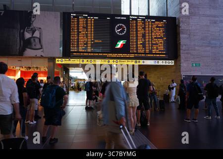 Les passagers se tiennent sous le grand tableau numérique de la gare Termini, suivant les horaires des trains et les mises à jour des quais dans un environnement bondé et rapide. Banque D'Images