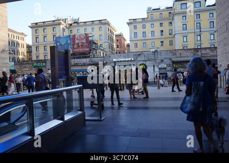 Vue extérieure depuis une sortie de station de métro, avec les gens marchant sur une place animée entourée de bâtiments historiques et de devantures de magasins modernes. Banque D'Images