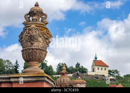 Vase ornemental en pierre et pittoresque petite église sur la colline contre le ciel bleu d'été, Prague, Tchéquie Banque D'Images