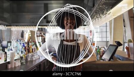 Mélange barman portant un tablier rayé versant le cocktail derrière le bar, avec terminal à écran tactile Banque D'Images
