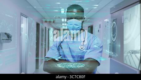 Médecin debout portant des gommages bleu clair et un masque dans le couloir de l'hôpital avec interface holographique Banque D'Images