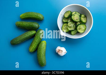 Salade de concombre finement tranchée garnie d'aneth frais, d'ail et de graines de sésame, servie dans un bol blanc sur fond bleu. Léger, sain et refr Banque D'Images