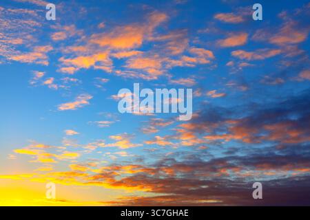 Ciel rayonnant au lever ou au coucher du soleil, passant du bleu au-dessus de l'horizon à l'horizon proche chaud. Les nuages éparpillés brillent avec de douces teintes rose et orange, Banque D'Images