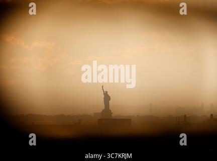 Brooklyn, États-Unis. 01 août 2025. Le ciel apparaît jaune autour de la Statue de la liberté lorsqu'il est photographié à travers une clôture en fil de fer avant le coucher du soleil le vendredi 1er août 2025 à New York. Photo de John Angelillo/UPI crédit : UPI/Alamy Live News Banque D'Images