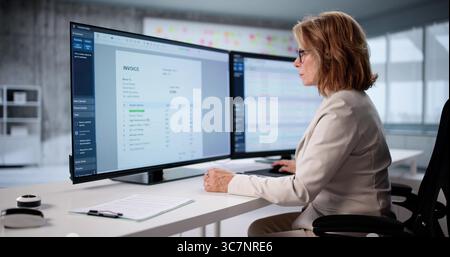 Le comptable principal étudie les codes financiers sur l'écran de l'ordinateur du siège social. Banque D'Images