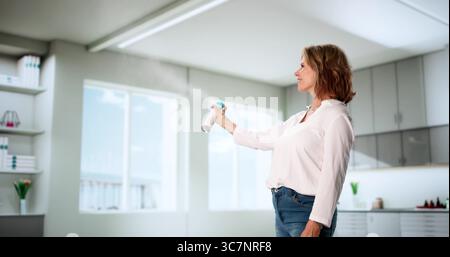 Femme pulvérisant le déodorant d'air frais dans l'odeur de tapis de salon Banque D'Images
