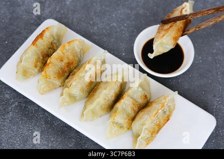 Une paire de baguettes trempant du Mandu ou des boulettes coréennes dans un petit bol de sauce soja foncée. Banque D'Images