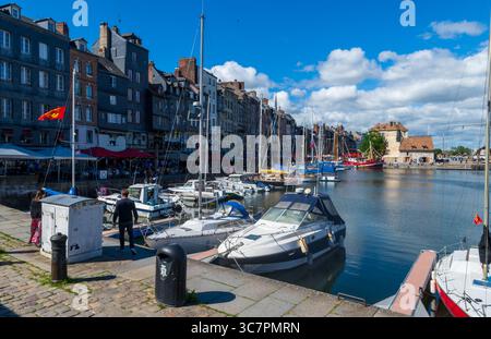 Port de Honfleur en Normandie, dans le nord de la France, avec des bateaux amarrés le long du quai, des bâtiments traditionnels à colombages et en pierre, et un ciel d'été lumineux Banque D'Images