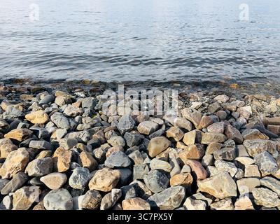 Le rivage du lac est recouvert de roches car l'eau vibre doucement contre eux. Banque D'Images