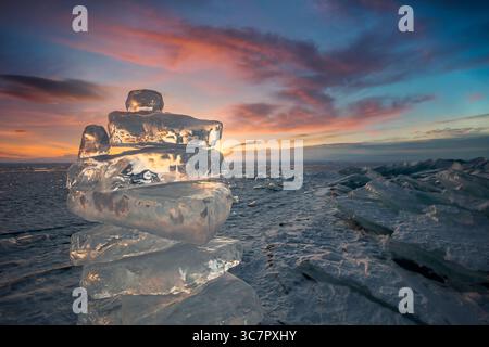 Coucher de soleil reflété dans un grand bloc de glace hummock sur l'arrière-plan du lac gelé. Banque D'Images
