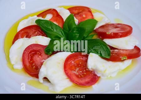 Salade Insalata Caprese avec Mozzarella di Bufala Campana, tomates rouges et feuilles de basilic vert habillées d'huile d'olive extra vierge Banque D'Images
