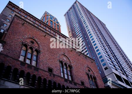 La façade historique en briques rouges d'une église néo-gothique se dresse sous les tours modernes vertigineuses le long d'un canyon de Manhattan sous un ciel bleu vif. Banque D'Images