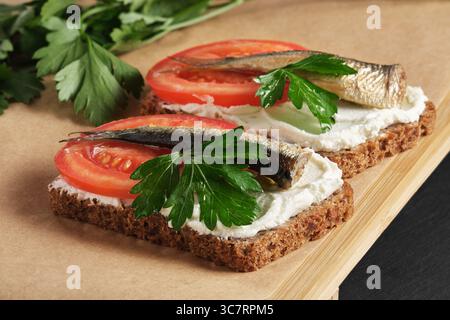 Sandwichs avec sprats, tomates et persil sur plateau de service en bois sur fond de pierre noire. Banque D'Images