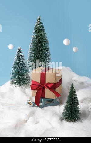 Boîte cadeau Kraft avec arc rouge sur traîneau à jouets. Composition hivernale. Banque D'Images