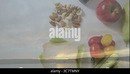 Affichage de noix, tranches de pain, fruits et légumes sur la surface de travail pâle, avec recouvrement de coucher de soleil sur le lac Banque D'Images