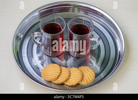 Deux tasses de thé noir ou rouge sur une assiette en acier avec quelques biscuits. Au Bangladesh, cela s'appelle Rong Cha ou Lal Cha. Le thé noir est également riche en antioxi Banque D'Images