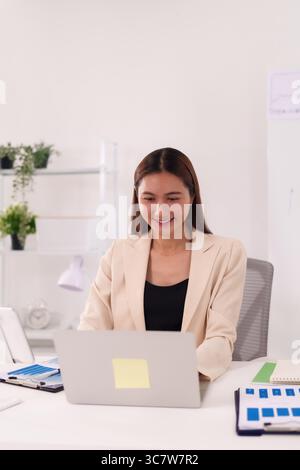 La femme adulte asiatique concentrée effectue diligemment des tâches de travail à distance sur ordinateur portable dans un environnement de bureau à domicile lumineux moderne assurant une opération numérique efficace Banque D'Images