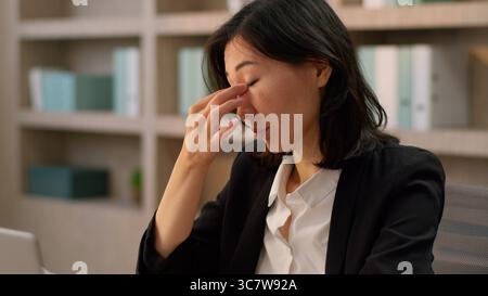 Femme d'affaires asiatique fille d'affaires travailler ordinateur portable au bureau chinoise japonaise se sentent mal de tête fatiguée épuisée femme coréenne surtravaillée souffrent Banque D'Images