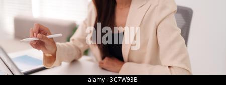 Gros plan adulte femme asiatique main tenant le stylet blanc stylet s'engageant avec la tablette numérique pour les tâches d'affaires ou les projets créatifs Banque D'Images