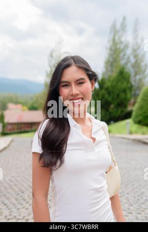 Belle jeune femme asiatique en polo marchant le long de la vieille rue de la ville de style européen. Portrait de voyage élégant entouré d'architecture, naturel ex Banque D'Images