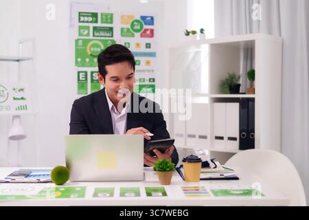Homme d'affaires asiatique positif effectue l'analyse des données de calculs financiers sur ordinateur portable. Il gère les rapports d'entreprise pour une croissance durable de l'entreprise. Banque D'Images