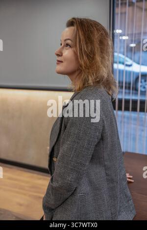 Woman Blazer Office : femme regarde soigneusement dans un bureau, portant un blazer, apparemment perdu dans la contemplation. Banque D'Images