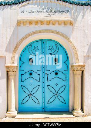 Porte bleue tunisienne traditionnelle avec des clous métalliques complexes et des murs blanchis à la chaux, symbolisant le charme méditerranéen et le patrimoine culturel de l'Afrique du Nord Banque D'Images