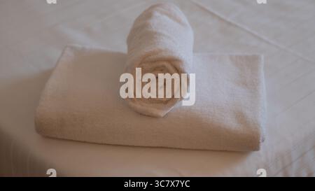 Serviette blanche roulée placée au-dessus d'une serviette soigneusement pliée sur un lit, créant une atmosphère propre et accueillante. Banque D'Images