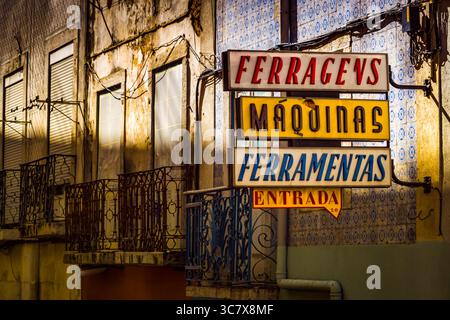 Enseigne de magasin vintage au néon pour la quincaillerie et les machines sur une façade de bâtiment altérée à Lisbonne, Portugal, avec des carreaux azulejos et des balcons en fer. Banque D'Images