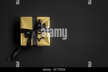 Bannière avec boîte cadeau dorée et ruban noir sur fond noir. Vue de dessus, copyspace. Banque D'Images