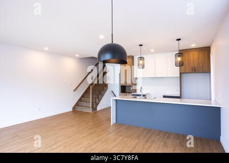 Un intérieur de maison moderne avec une cuisine élégante, un coin repas, un salon et un escalier menant à l'étage supérieur. Banque D'Images