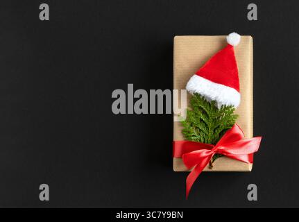 Boîte cadeau artisanale avec arbre de noël en thuya et chapeau de père noël sur fond sombre avec de l'espace pour votre texte. Banque D'Images