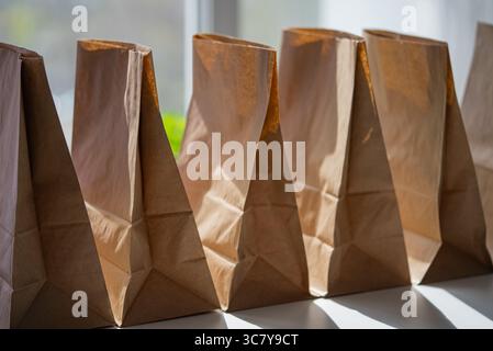 La lumière du soleil qui coule à travers une fenêtre met en évidence les sacs d'épicerie vides en papier brun, debout ouvert sur une table, attendant patiemment d'être rempli pour les livraisons à venir Banque D'Images