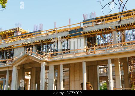 Sous un ciel ensoleillé, un bâtiment de plusieurs étages en béton est sous Un grand bâtiment en béton est en cours de construction, avec échafoldin Banque D'Images