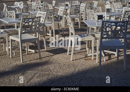 Rangées de chaises décoratives contemporaines avec des motifs géométriques disposées sur les tables de café sur la place en pierre dans la lumière chaude du soleil Banque D'Images
