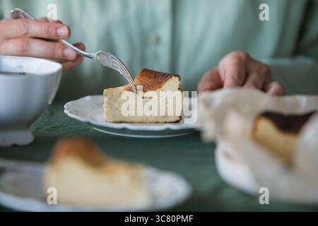 Gros plan d'une femme mangeant une tranche de cheesecake basque à faible teneur en glucides fait maison avec une tasse de café Banque D'Images