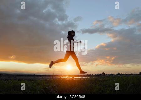 Vue latérale pleine longueur d'une jeune femme faisant du jogging à travers un paysage rural au coucher du soleil, Thaïlande Banque D'Images