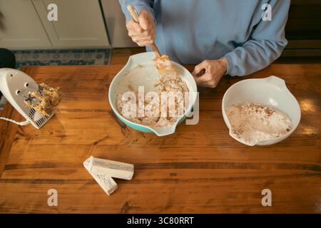 Vue aérienne d'une femme âgée debout dans une cuisine mélangeant la pâte à biscuits dans un bol avec une spatule Banque D'Images