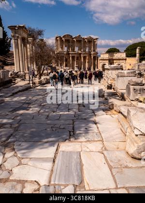 Un groupe de touristes marchent le long d'un chemin de pierre vers la bibliothèque de Celsus à Éphèse, en Turquie, explorant les ruines antiques et apprenant l'histoire du site. Banque D'Images