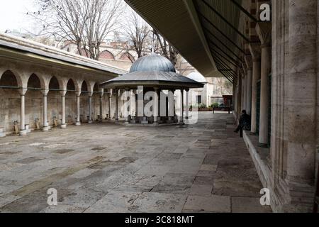 Une personne est assise le long du mur de la cour de la Mosquée bleue à Istanbul, Turquie. Banque D'Images
