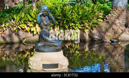 Melbourne, Victoria, Australie - 20 juillet 2025 : sculpture de nymphe d'eau en bronze dans un étang entouré de plantes feuillues et de reflets Banque D'Images