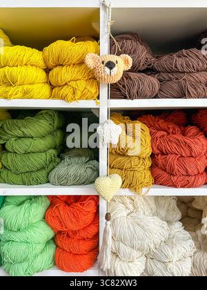 assortiment vibrant de laine, de mélange de laine et de fils de coton de différentes couleurs soigneusement disposés sur des étagères blanches propres avec suspension de jouet tricoté fait à la main Banque D'Images