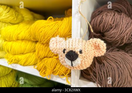 assortiment vibrant de laine, de mélange de laine et de fils de coton de différentes couleurs soigneusement disposés sur des étagères blanches propres avec suspension de jouet tricoté fait à la main Banque D'Images