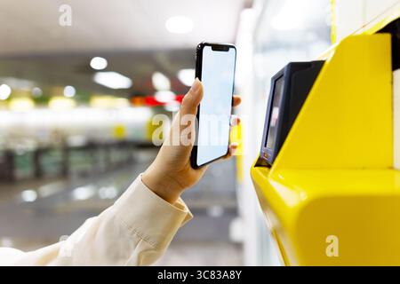 Femme utilisant le téléphone portable pour payer l'achat au distributeur automatique de boisson à la station de métro, technologie et concept de paiement sans contact. Banque D'Images