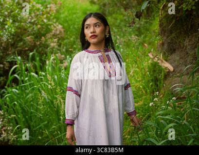 Une jeune femme indigène portant des vêtements traditionnels explore une végétation luxuriante, embrassant son patrimoine culturel et son lien avec la nature Banque D'Images