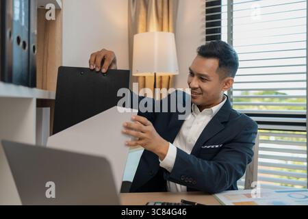 homme d'affaires professionnel d'âge moyen portant chemise blanche et costume joyeusement souriant dans le bureau, un homme d'affaires d'âge moyen, cheveux foncés dans un costume est heureux Banque D'Images