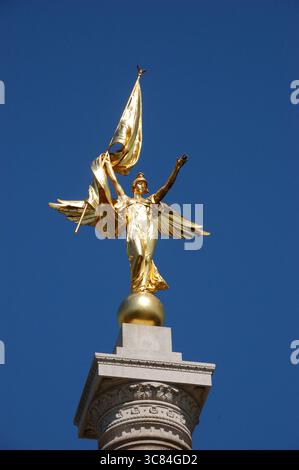 Statue dorée d'une figure féminine ailée tenant un drapeau, debout au sommet d'une haute colonne contre un ciel bleu clair à Washington, D.C. Banque D'Images
