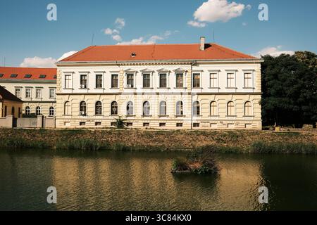 Vue sur la rivière d'un bâtiment jaune et blanc néoclassique à Zrenjanin, Serbie. Architecture élégante avec fenêtres cintrées reflétées dans l'eau calme. Banque D'Images