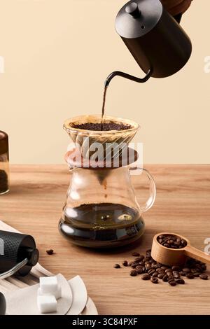 Versez sur le processus de préparation du café fraîchement infusé dans une servante en verre, le café se versant dans une cafetière geyser sur une table en bois Banque D'Images